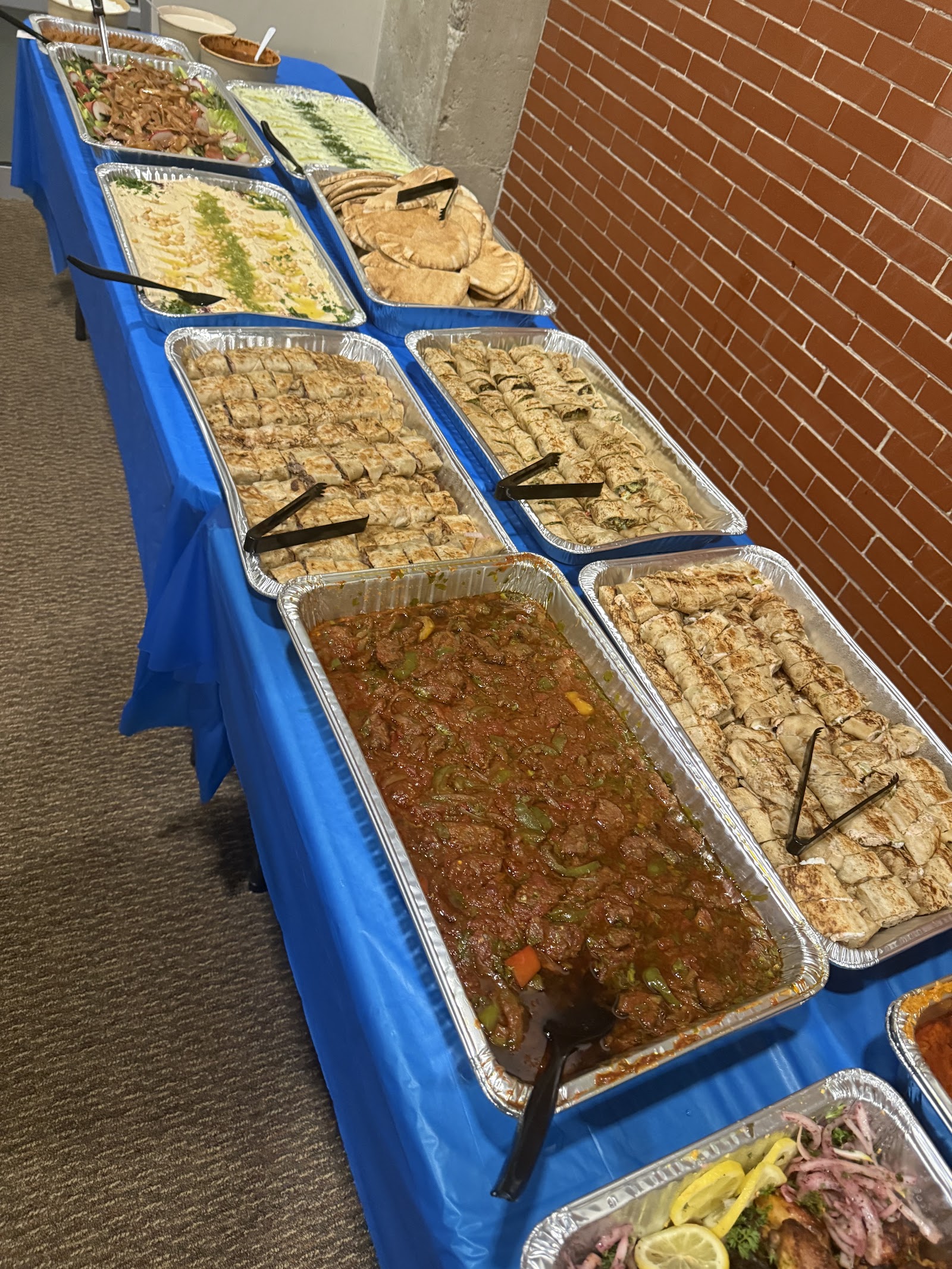 Catering buffet with hummus, pita, wraps and a tray of stew