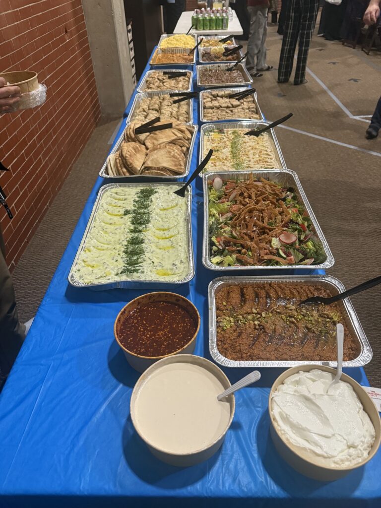 Catering buffet with salads, dips, pita and a tray of kunafeh