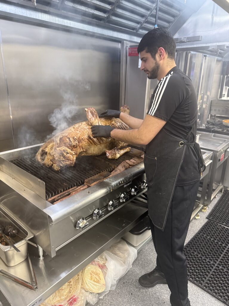 Chef grilling a whole lamb over an open flame in the kitchen